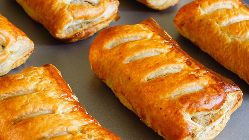 Freshly baked sausage rolls made with puff pastry fresh out of the oven cooling on a tray